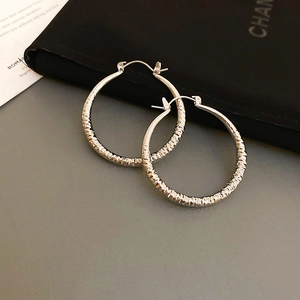 Macro detail of silver hoop earrings featuring irregular hammered texture and metallic finish