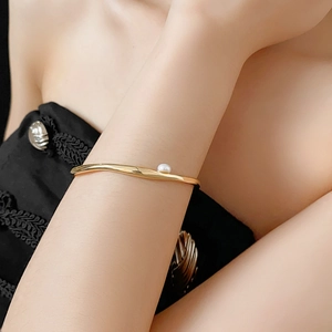 Close-up of elegant gold geometric bangle featuring a white pearl on a woman's wrist