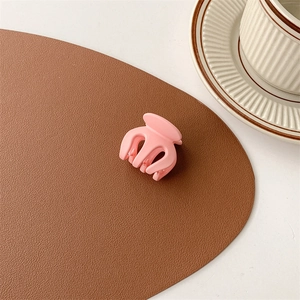 Detailed view of small matte pink hair claw clip on brown leather and coffee cup background