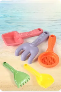 Close-up of candy-colored beach toy set with 5 pieces of plastic shovels and rakes on sand