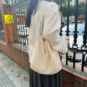 Close-up of a large beige checkered canvas tote bag with a woven brand tag on side