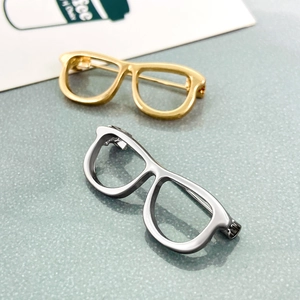 Minimalist gold and silver eyeglasses shape brooches on a textured background