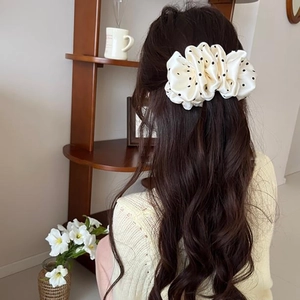 Creamy white polka dot bubble scrunchie worn on long wavy hair in a cozy home setting