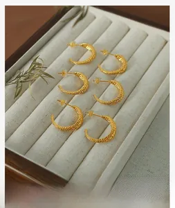Detail of three pairs of C-shaped hammered gold earrings on a beige velvet jewelry tray