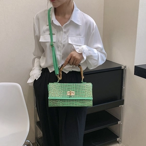 Green faux crocodile skin handbag with bamboo handle shown as a stylish crossbody bag