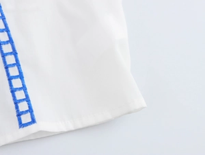 Detailed close-up of blue geometric embroidery on white textured fabric for summer set