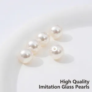 Five round ivory glass pearls with through-holes arranged on a white ceramic plate