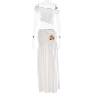 White two-piece set featuring a one-shoulder crop top and long skirt with gold metal flower