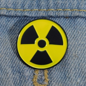 Macro shot of circular yellow and black radioactive symbol enamel pin on denim fabric