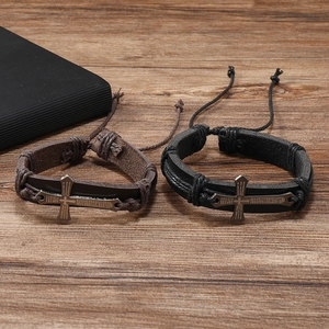 Close-up of black and brown leather braided bracelets with cross charm on wood