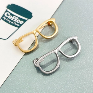 Minimalist hollow eyewear brooches in gold and silver metal finishes shown from top view