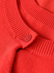 Detail of red knit jacket showing ribbed crew neck collar and matching resin button