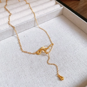 Dettaglio macro della collana con serpente dorato, anello traslucido e catena a forma di Y