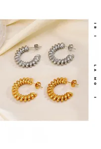 Détail de boucles d'oreilles créoles torsadées en or et argent sur soie beige