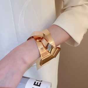 Close-up of a wide polished gold knotted cuff bracelet styled with a cream blazer