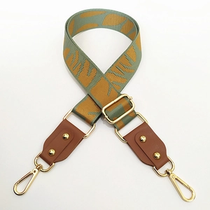 Detail of jacquard leaf pattern bag strap with brown leather and gold metal hooks