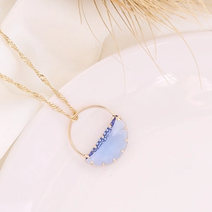 Elegant gold necklace with a blue crescent gemstone pendant on a white ceramic tray