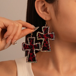 Close-up of red leopard print cross earrings with sparkling rhinestones worn by a model
