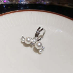 Macro detail of silver pearl ear cuff with zircon accents on white ceramic plate