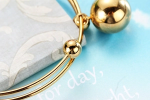 Detailed macro of a polished gold-plated double-layer bangle with spherical pendants