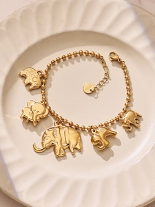 Détail d'un bracelet doré à perles avec des breloques éléphant sur un plateau blanc