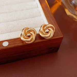Detail of gold knot earrings resting on a wooden jewelry box with a warm ambiance
