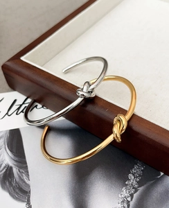 Detail view of gold and silver knot cuff bracelets on a wooden display tray