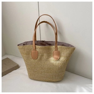 Close-up of large straw tote bag with brown leather handles and woven texture details