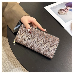 Detail of a brown herringbone woven long wallet with gold zipper on a black table