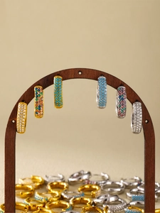 Detailed close-up of gold and silver hoop earrings with turquoise and zircon on wood stand