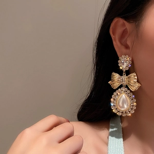 Gros plan de boucles d'oreilles nœud doré avec perle goutte et strass brillants