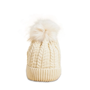 Close-up of cream cable knit texture and soft faux fur pom-pom on winter beanie hat