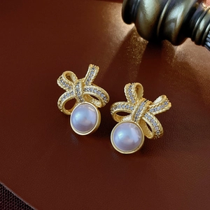Macro shot of gold bow stud earrings with white pearl and crystals on brown leather