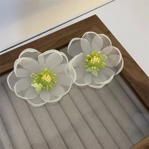 Macro detail of handmade white mesh floral earrings with yellow and green bead centers