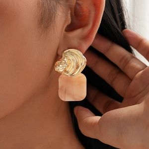 Close-up of textured gold metal and beige resin square earrings on a female model