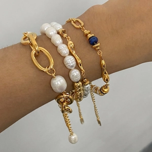 Detail of layered gold bracelets with baroque pearls and blue bead on model wrist