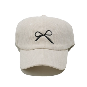 Close-up of beige corduroy baseball cap featuring black embroidered bow detail