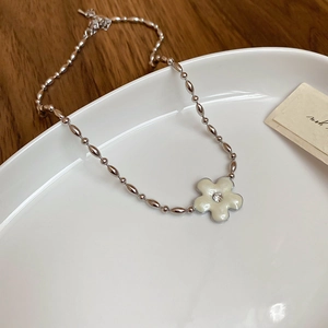 Detail of silver flower necklace with white petals and zircon on a ceramic plate