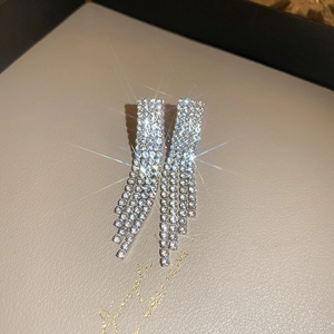 Dettaglio di orecchini a nappa in argento scintillante con strass su sfondo di pelle