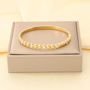 Primo piano di un bracciale rigido in acciaio inossidabile dorato con cristalli su supporto
