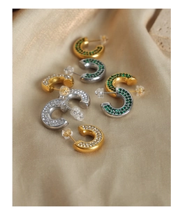 U-shaped gold and silver earrings with colorful zircon stones on beige silk fabric