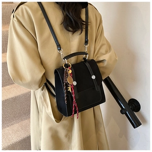 Detalle de bolso bandolera retro negro con anillo metálico y colgante de pluma en gabardina