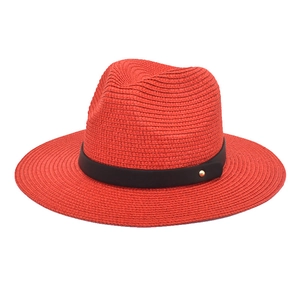 Close-up of vibrant red woven straw sun hat with black ribbon and gold rivet detail