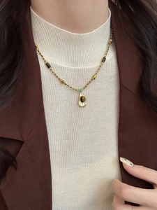 Détail d'un collier vintage doré avec une pierre oeil de tigre brune et perle verte