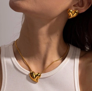 Polished gold-plated heart pendant necklace and matching stud earrings worn by a model