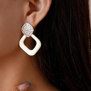 Close-up of geometric earrings with silver hammered metal and white square resin pendant