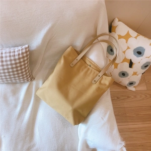 Yellow canvas tote bag with cream straps styled on a white blanket for a cozy daily look