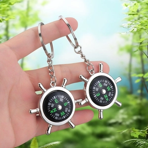 Silver helm compass keychain with functional dial shown in a scenic outdoor setting