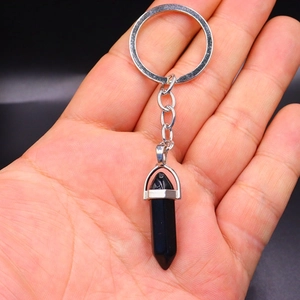 Hand holding a double-pointed black obsidian hexagonal crystal bullet keychain