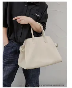 Close-up of beige leather tote bag featuring side buckle straps and round handles